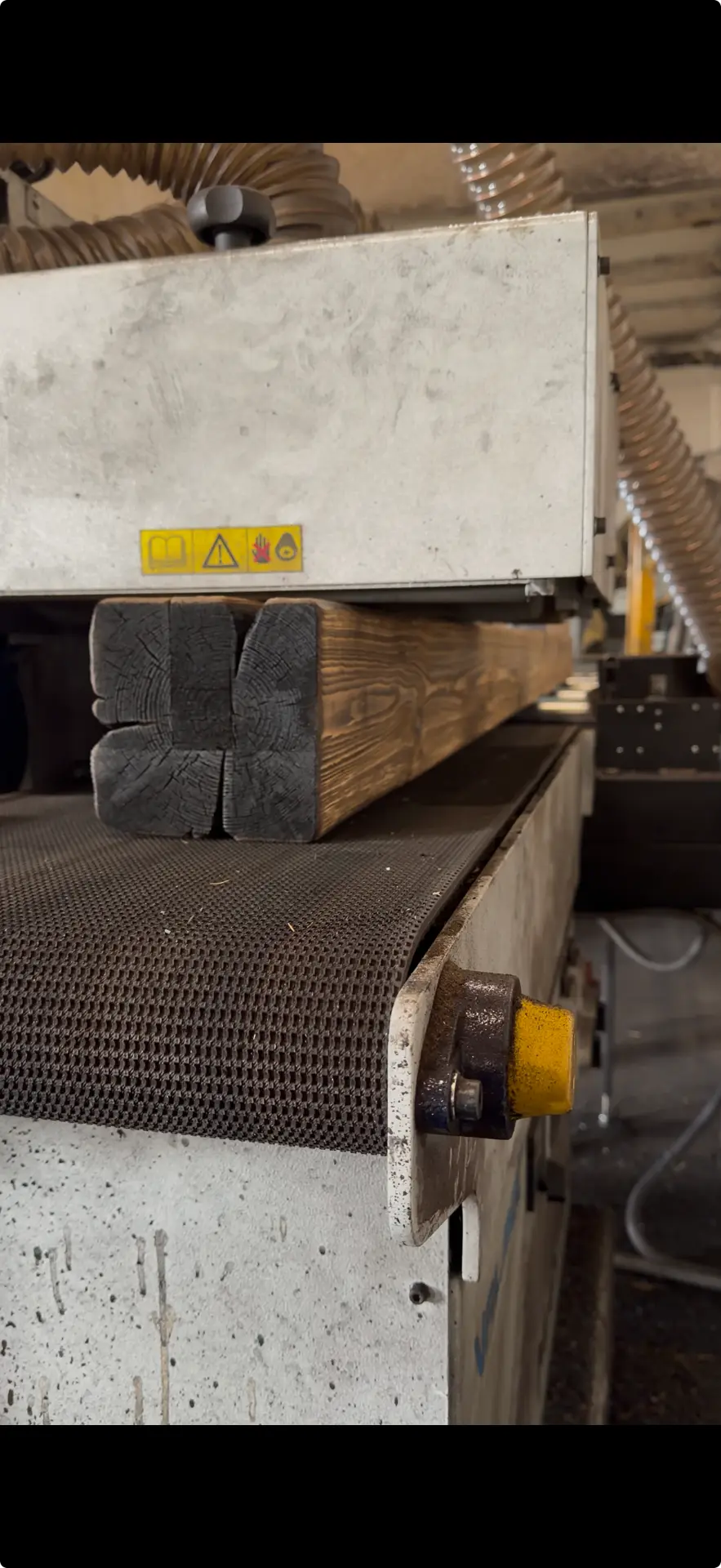 Charred timber boards passing through industrial brushing equipment at the Inflamed factory